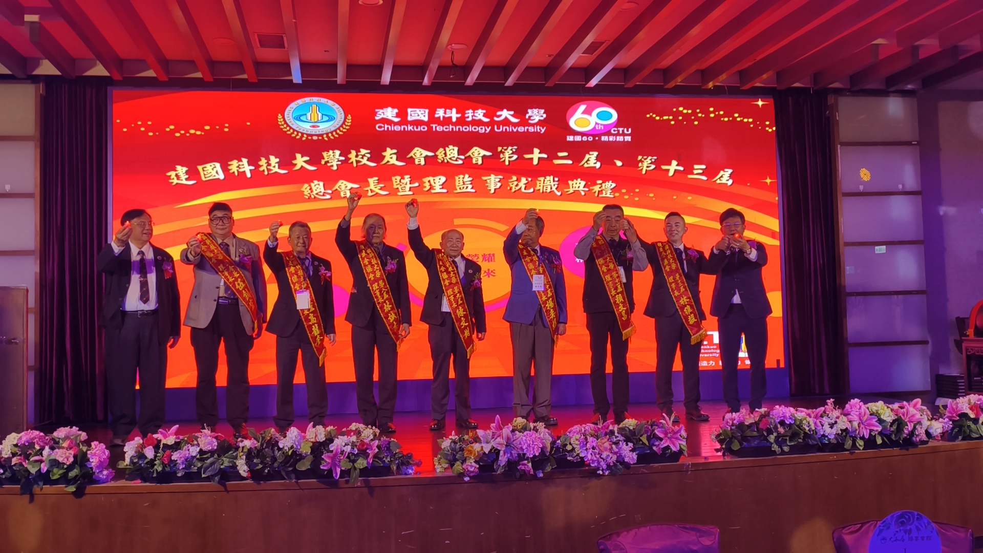 建國科技大學校友總會舉行理事長交接典禮，新、卸任理事長與歷屆幹部齊聚台上合影舉杯祝賀，場面隆重熱烈，象徵校友傳承與團結向心力。